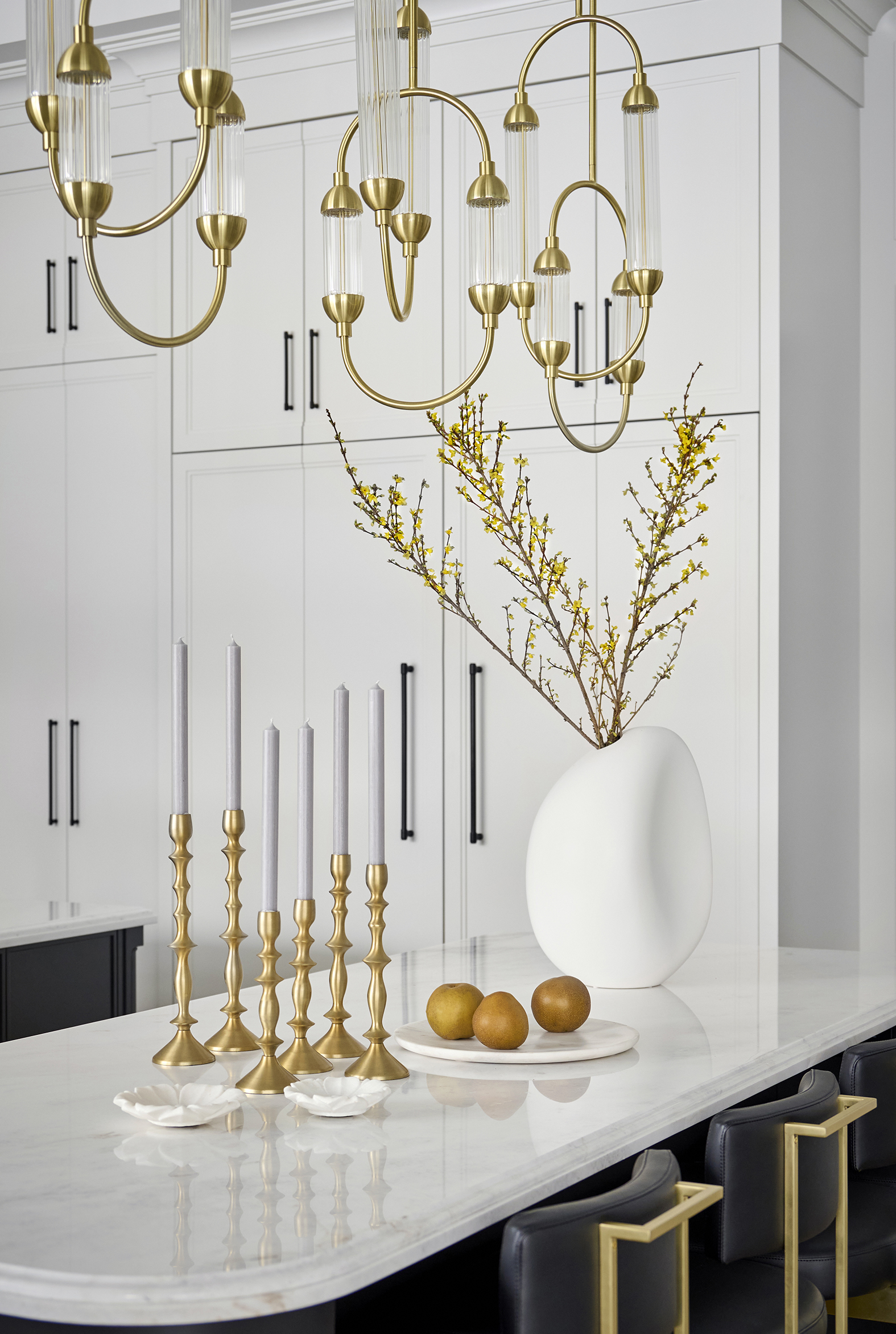 White marble top kitchen island with golden candle holders, a white vase and golden chandelier